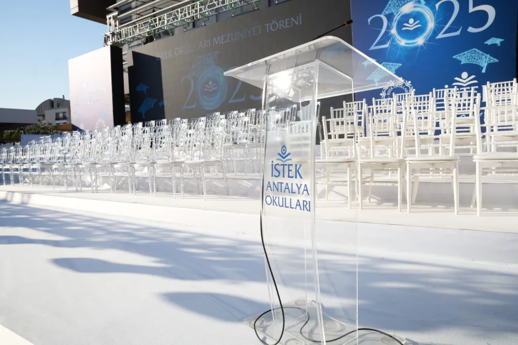 Clear acrylic lectern with İSTEK Antalya Schools branding at an open-air graduation ceremony