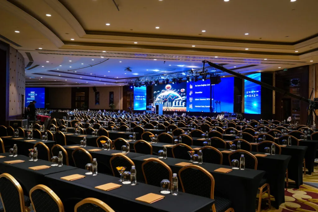 Classroom-style conference set-up with truss stage, LED screens and camera crane in a hotel ballroom, Türkiye