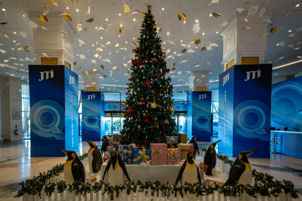 Branded column wraps with Christmas tree and penguin décor in a hotel lobby for a JTI event, Türkiye