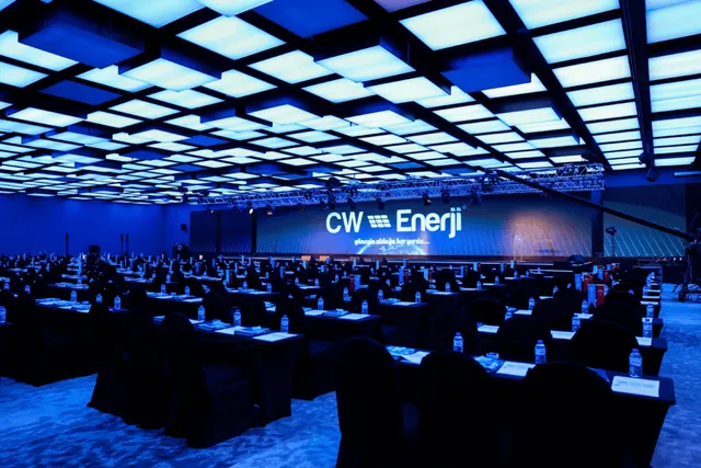 Plenary conference room in classroom set-up under a blue lit ceiling with stage screens for the CW Enerji dealer meeting in Antalya