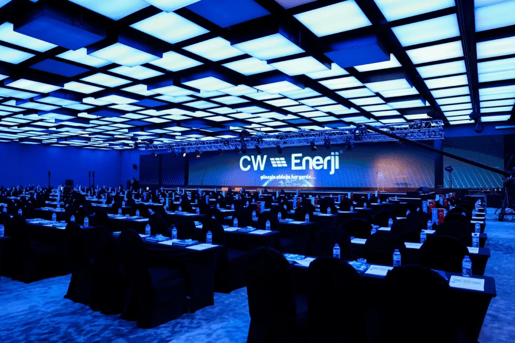 Plenary conference room in classroom set-up under a blue lit ceiling with stage screens for the CW Enerji dealer meeting in Antalya